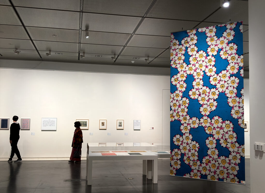 Exhibition gallery with large tapestries featuring modern cherry blossom and mushroom motifs